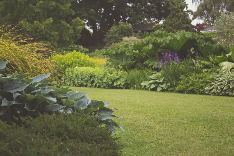 A large two-storey brick house with a pitched red tile roof, featuring multiple rectangular and bay windows with dark frames, surrounded by a well-maintained garden. The garden includes a neatly trimm